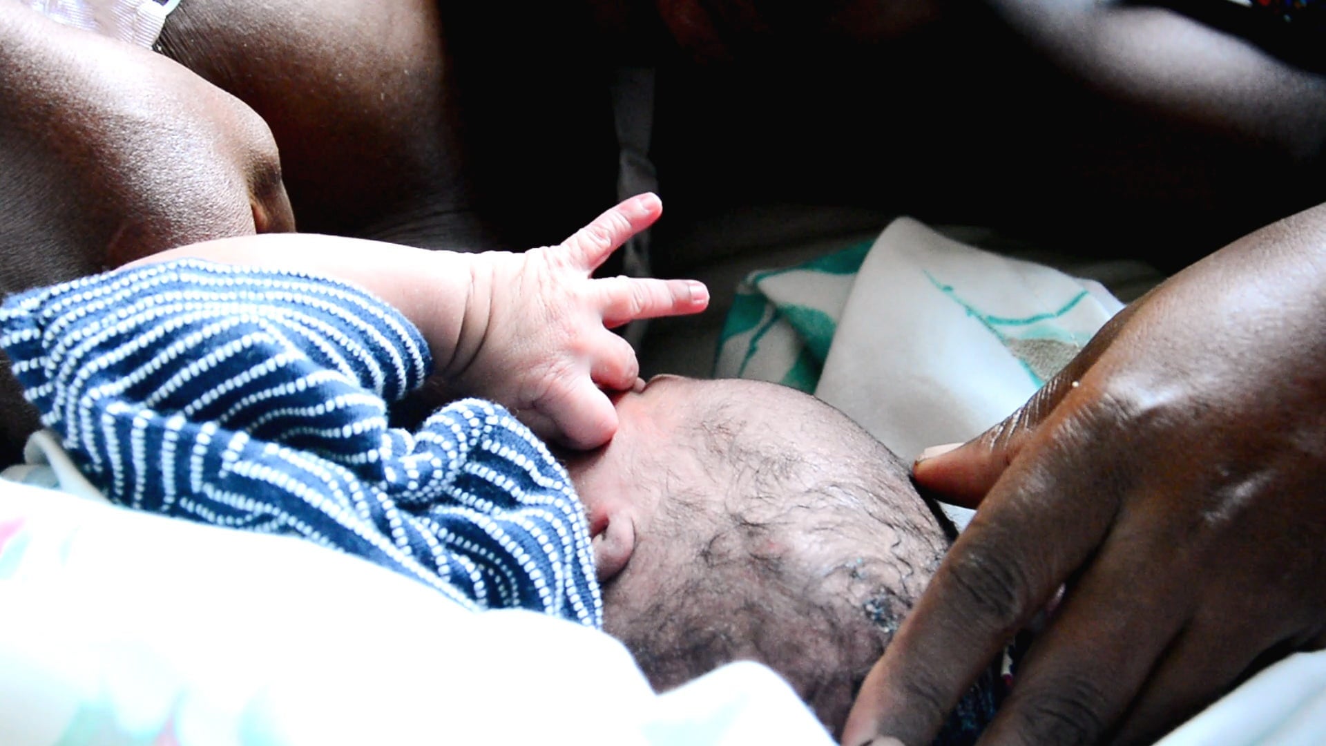 A mother lies next to her newborn child, cradling its head.