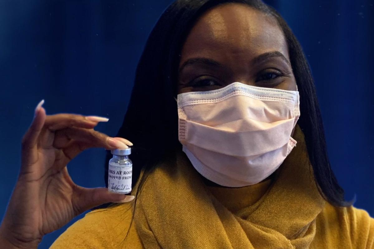 Kizzmekia Corbett wearing a mask and holding a covid vaccine shot in her hand