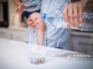 Parent holding child pouring bottled water into a glass