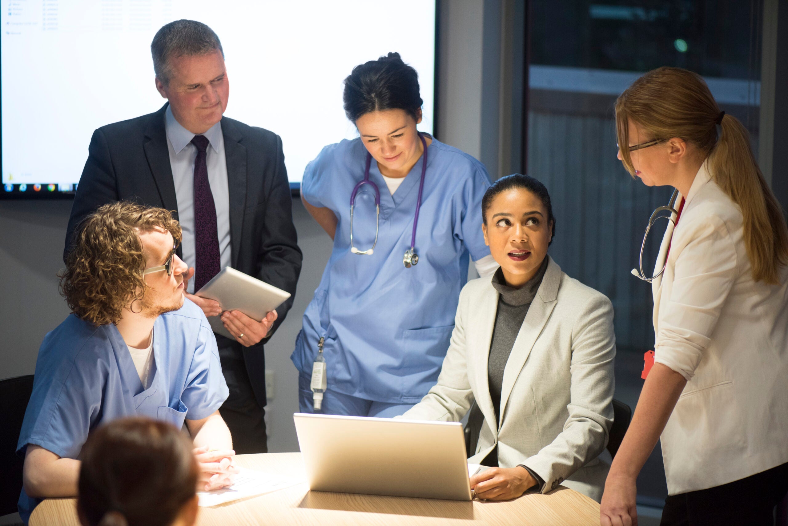 A group of businesspeople and clinicians surrounding a table in an office room.