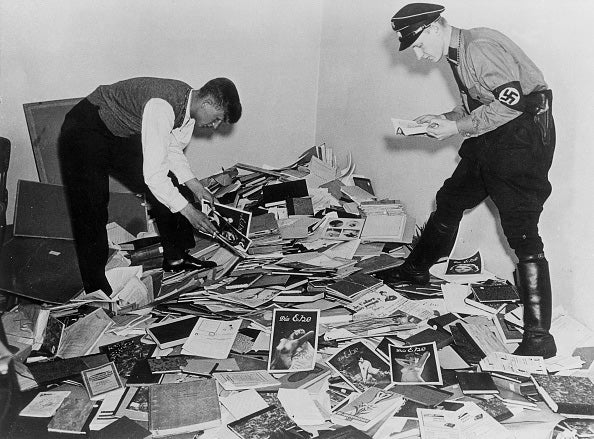 Nazi officials sort through a large pile of papers, pamphlets, books and photos scattered on the floor from the Institute for Sexual Science, to be burned.