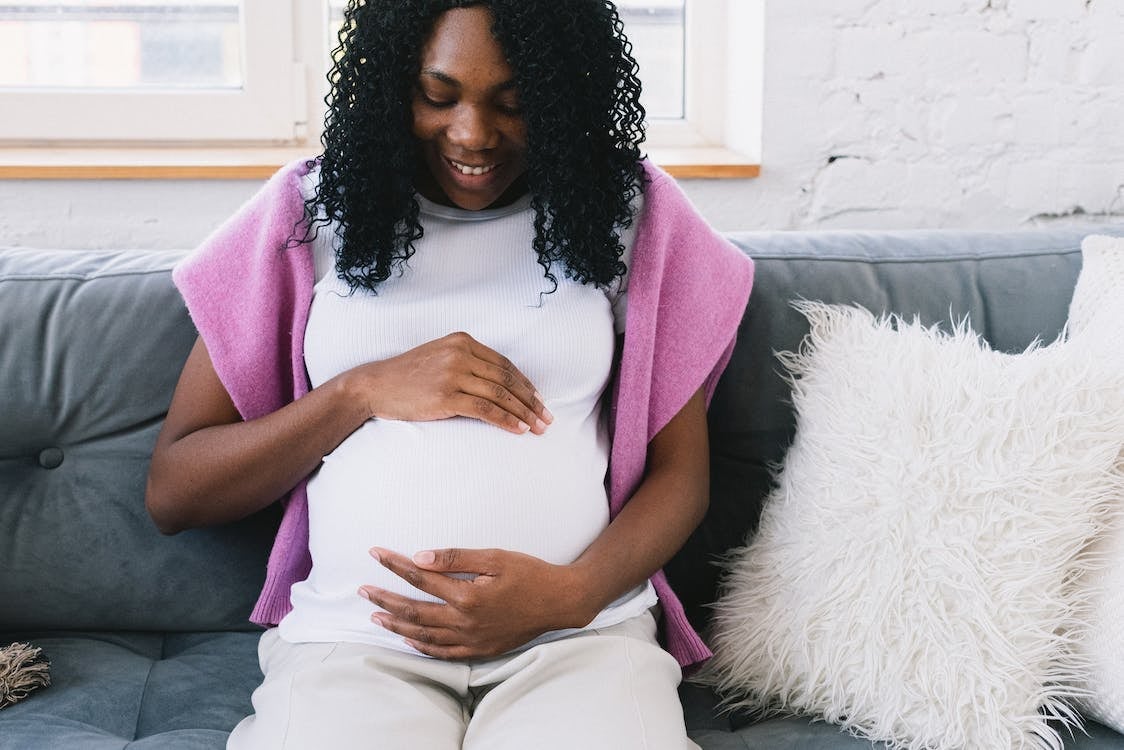 Pregnant person sitting on a coach cradling their belly and smiling.