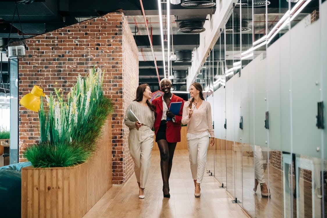 Three business women smiling and talking as they walk down the hallway of an office building