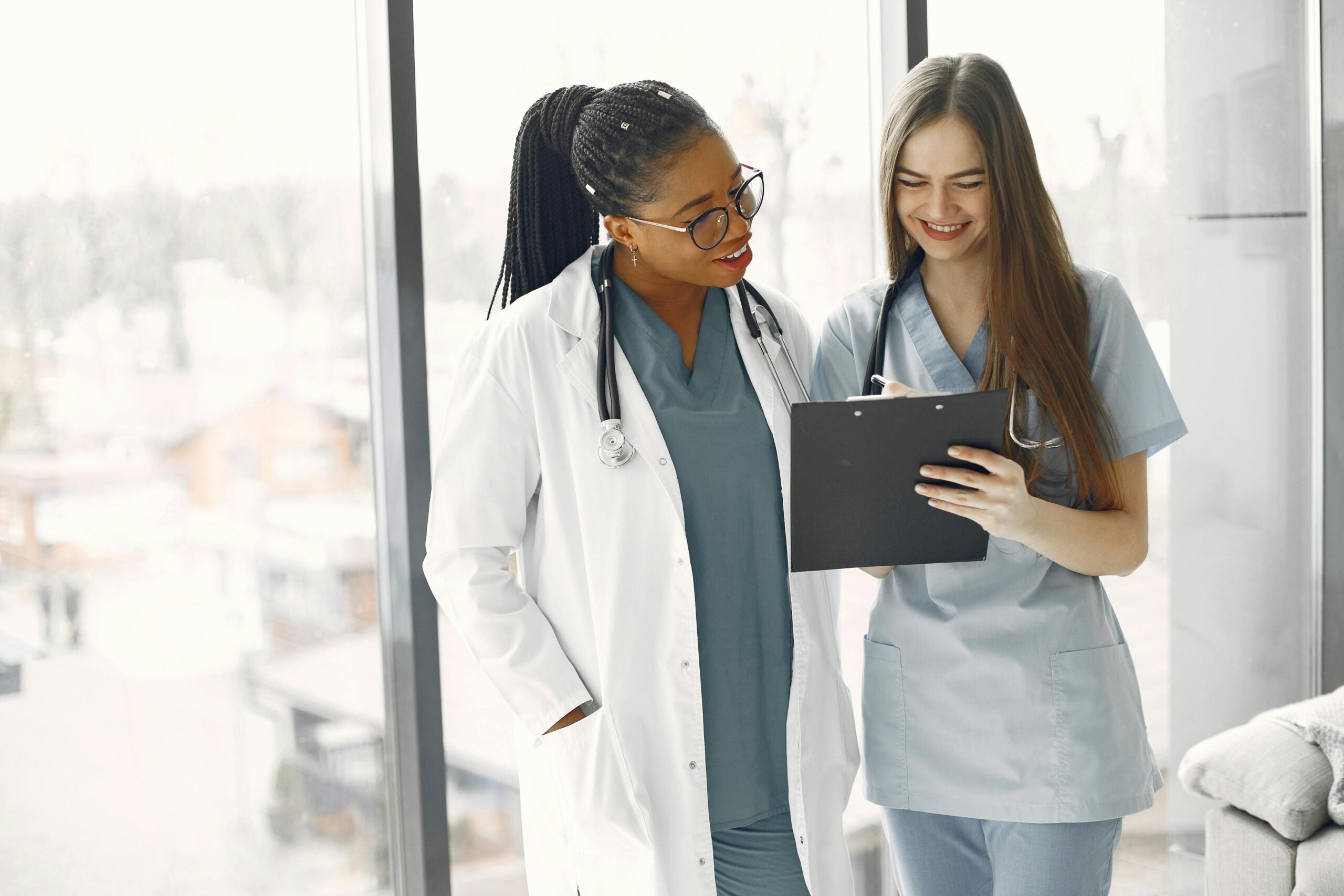 A nurse and doctor standing front of a window, smiling as they look over patient notes.