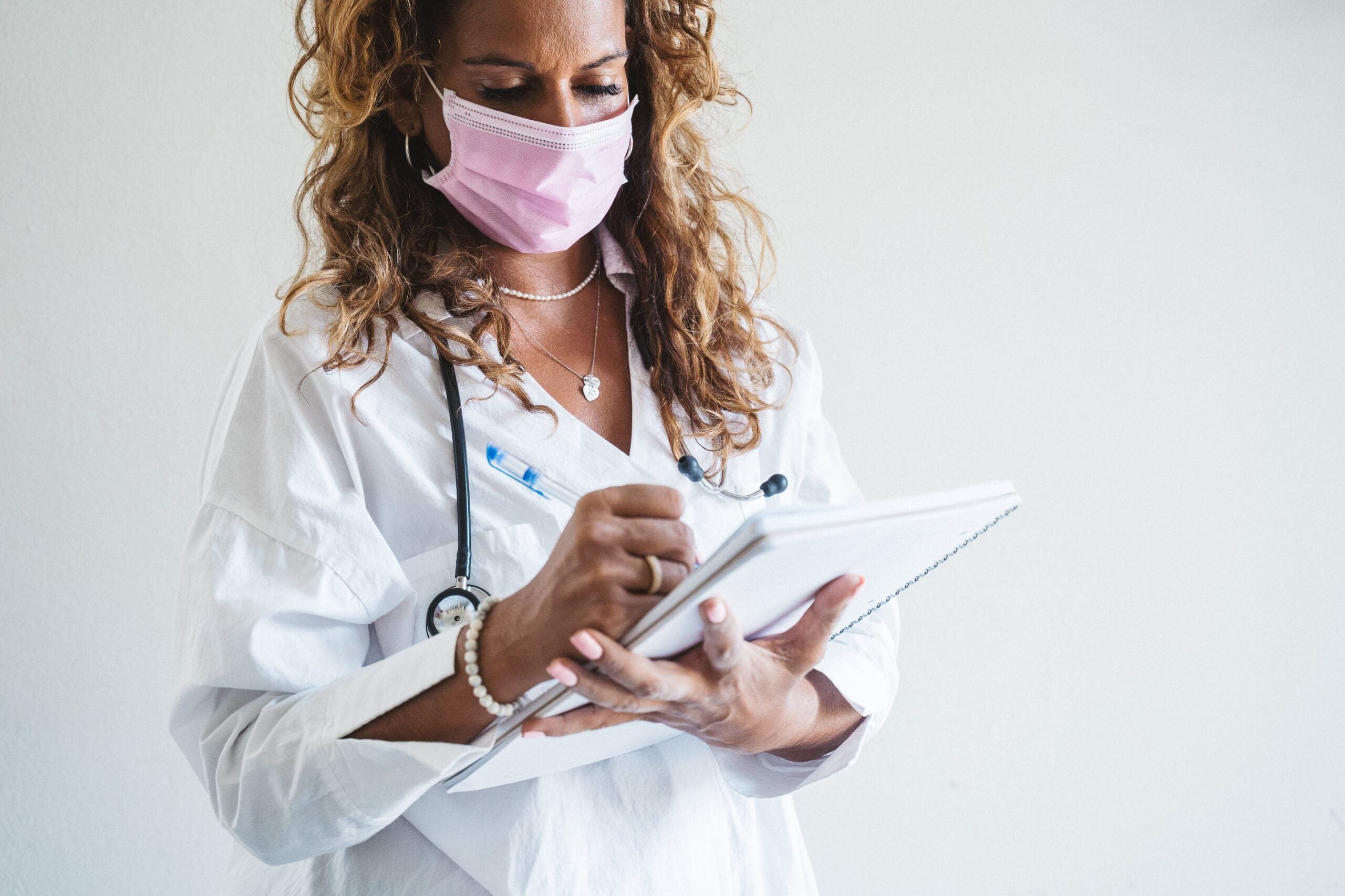 Female doctor wearing a mask writing on a notebook.