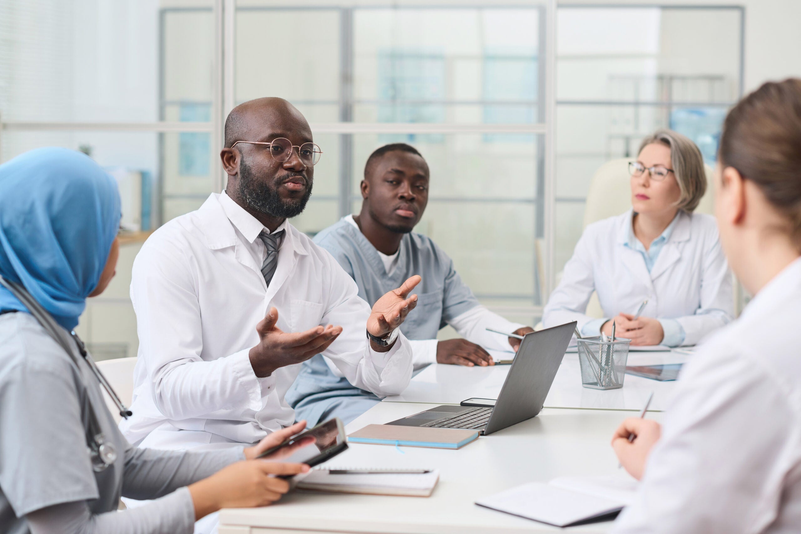 A group of doctors and health professionals seated at a table, listing to the head doctor.