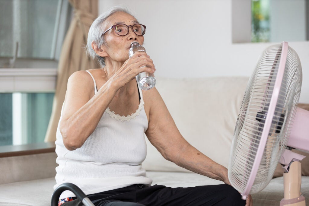 Older woman drinks water in front of a fan