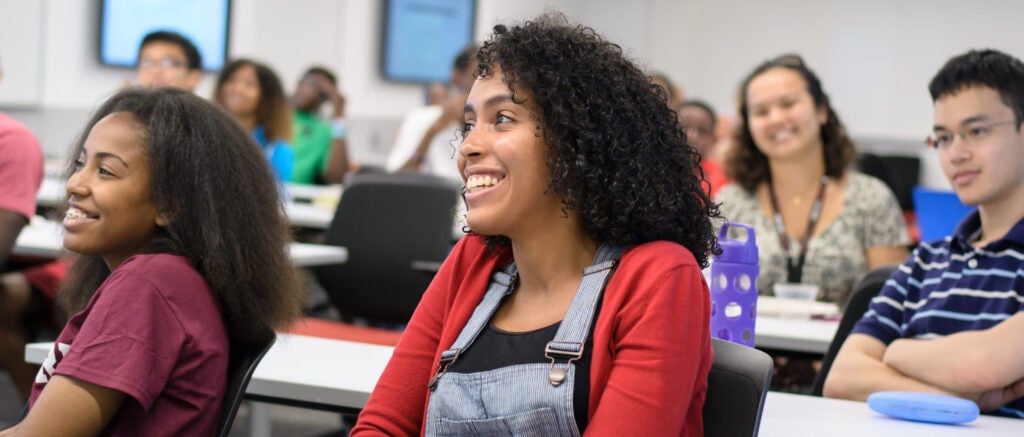 Students sitting in a seminar room, smiling at a teacher out of frame.