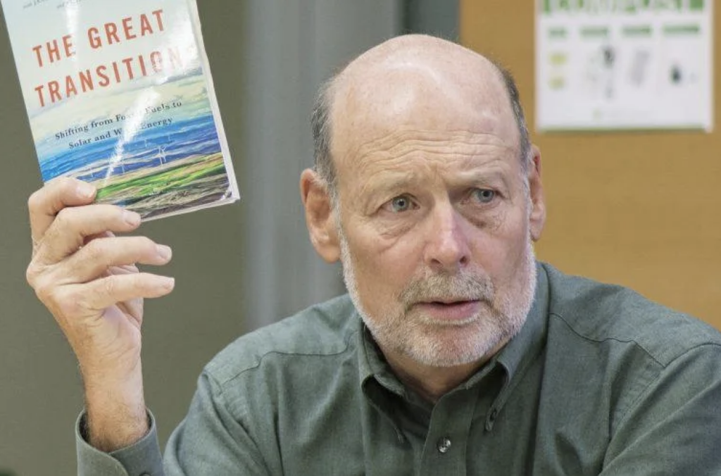 Professor Jack Spengler holding up a book titled 'The Great Transition, gesturing to highlight its significance