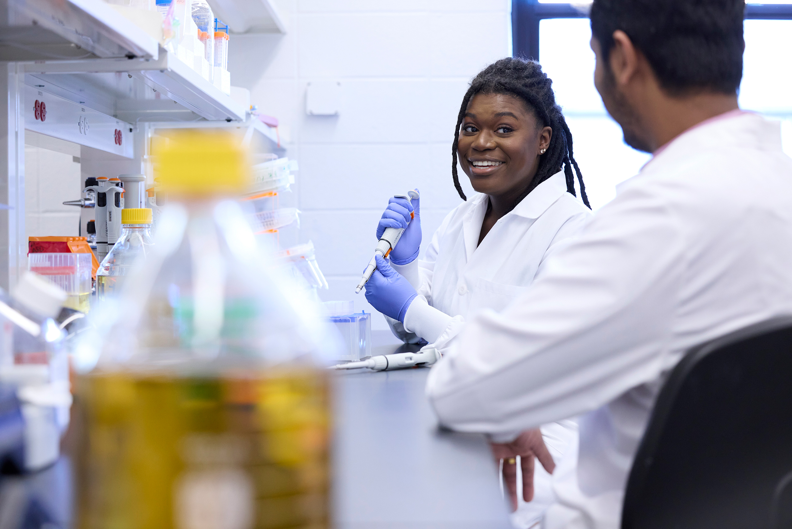 Abigail Dzordzorme,former lab member, talking to Jeswin Joseph while working in the lab