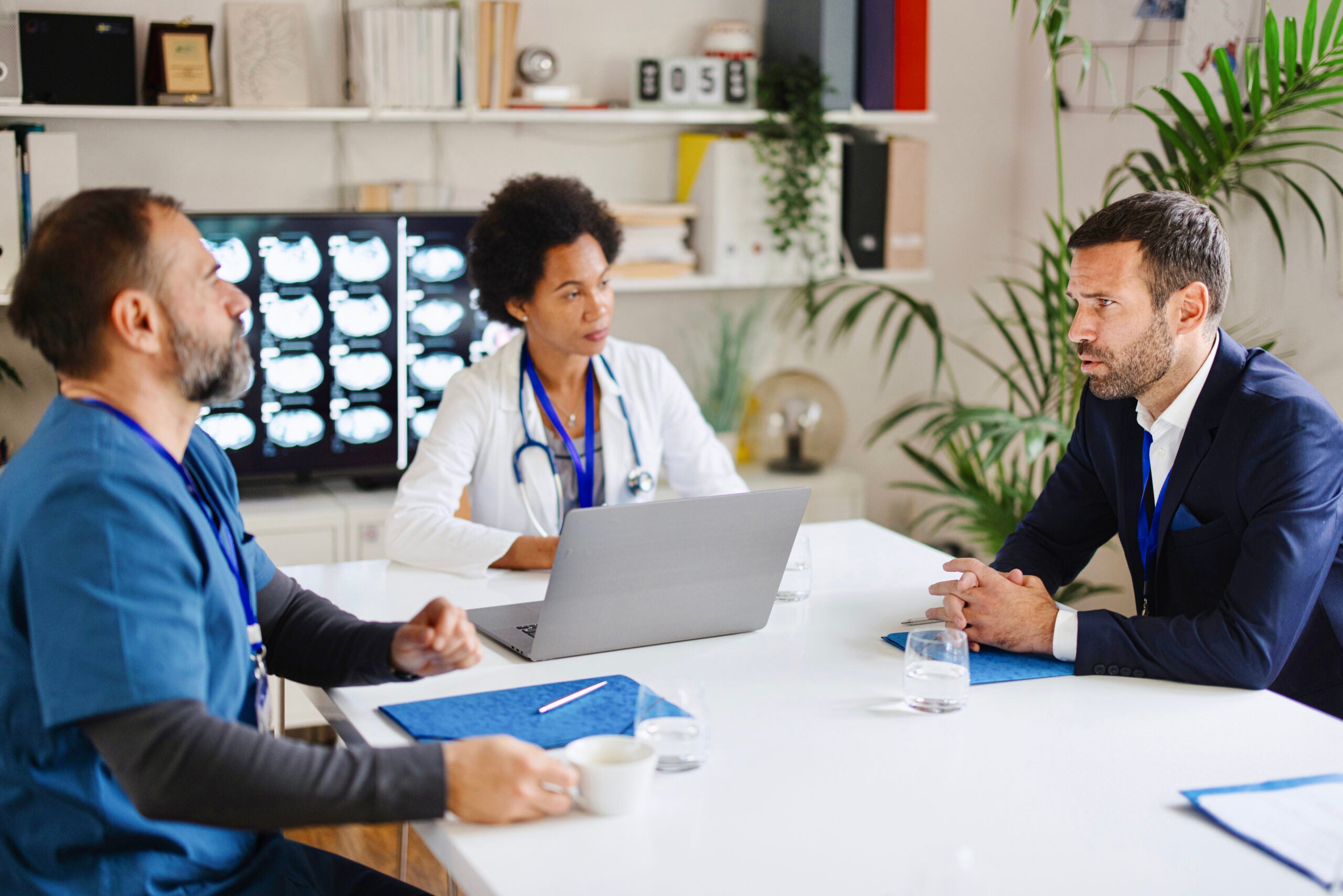 A doctor, nurse, and executive are sitting in a board room having an intense discussion