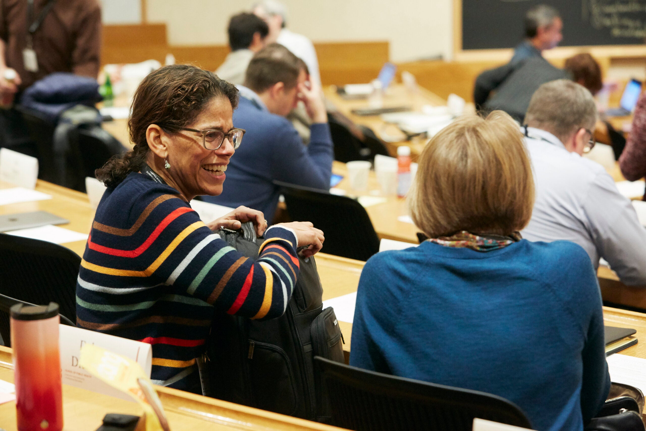 Two participants sitting in a Harvard Chan classroom, talking to one another and smiling