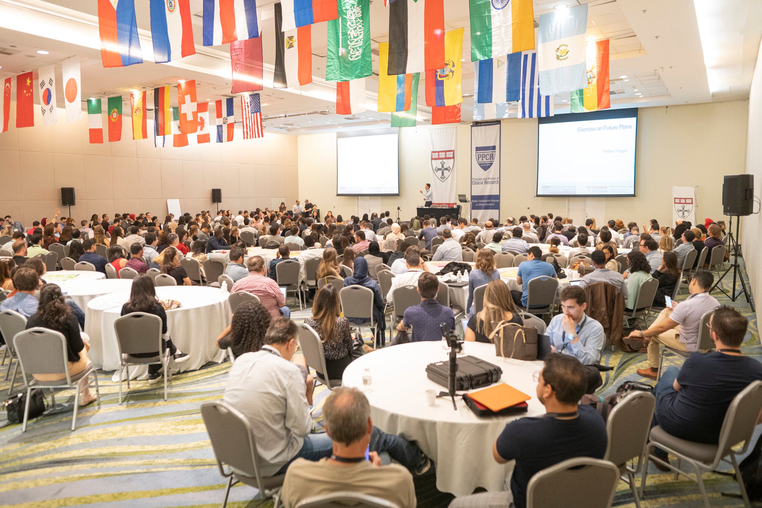 Conference room with PPCR students sitting at tables. Flags from across the world are hanging from the ceiling