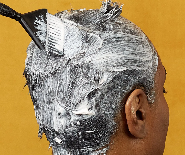 A woman at a salon having relaxer applied to her hair.