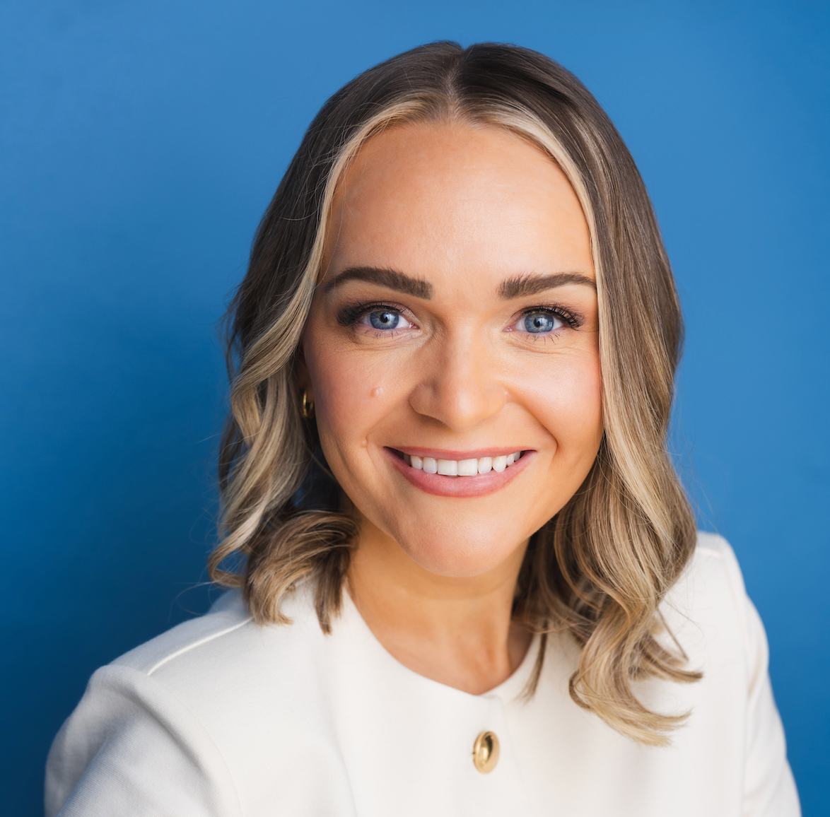 Headshot of Emily Mckinley wearing a white blazer against a blue background.