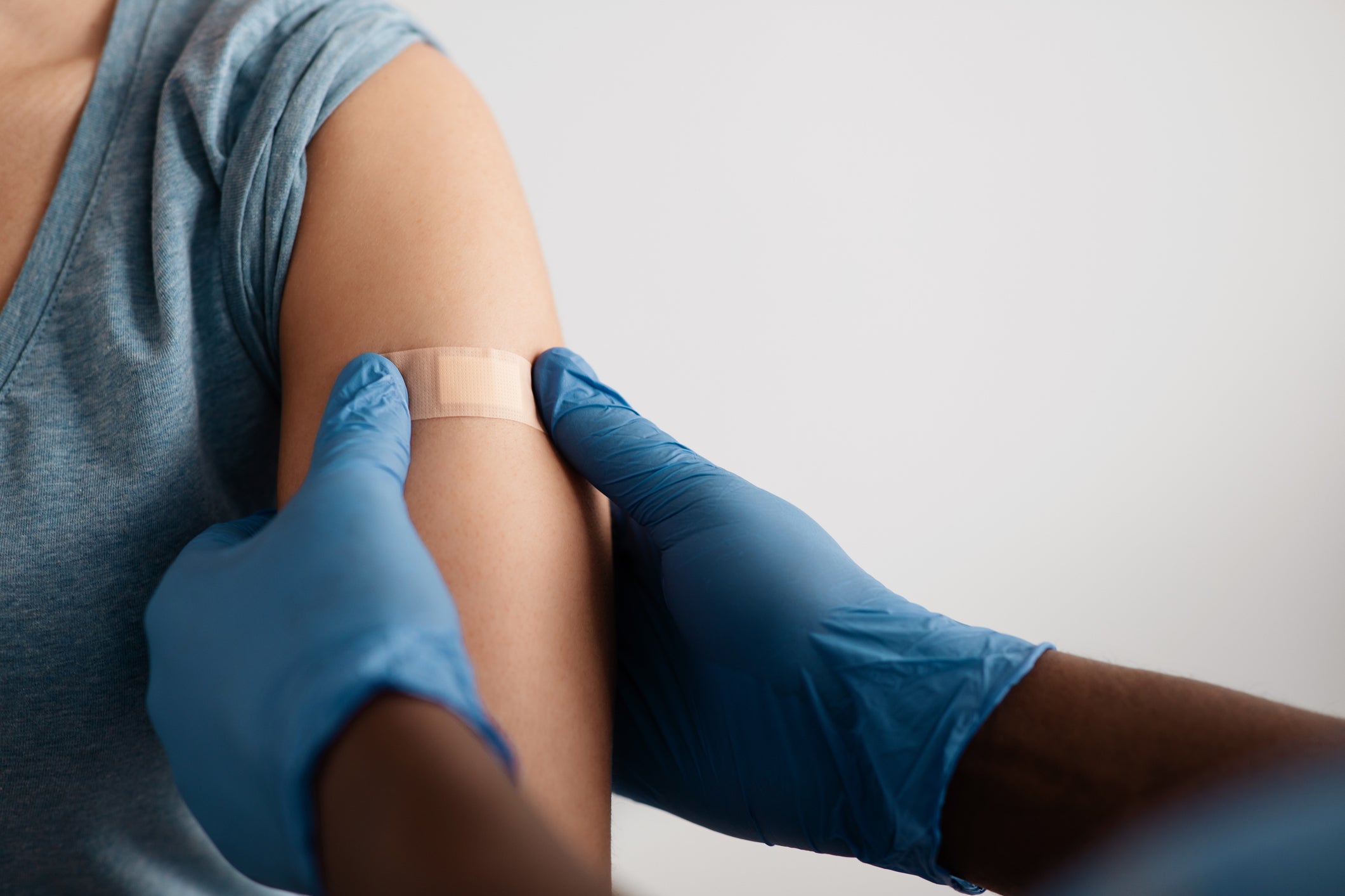 closeup of two gloved hands putting a band-aid on an arm