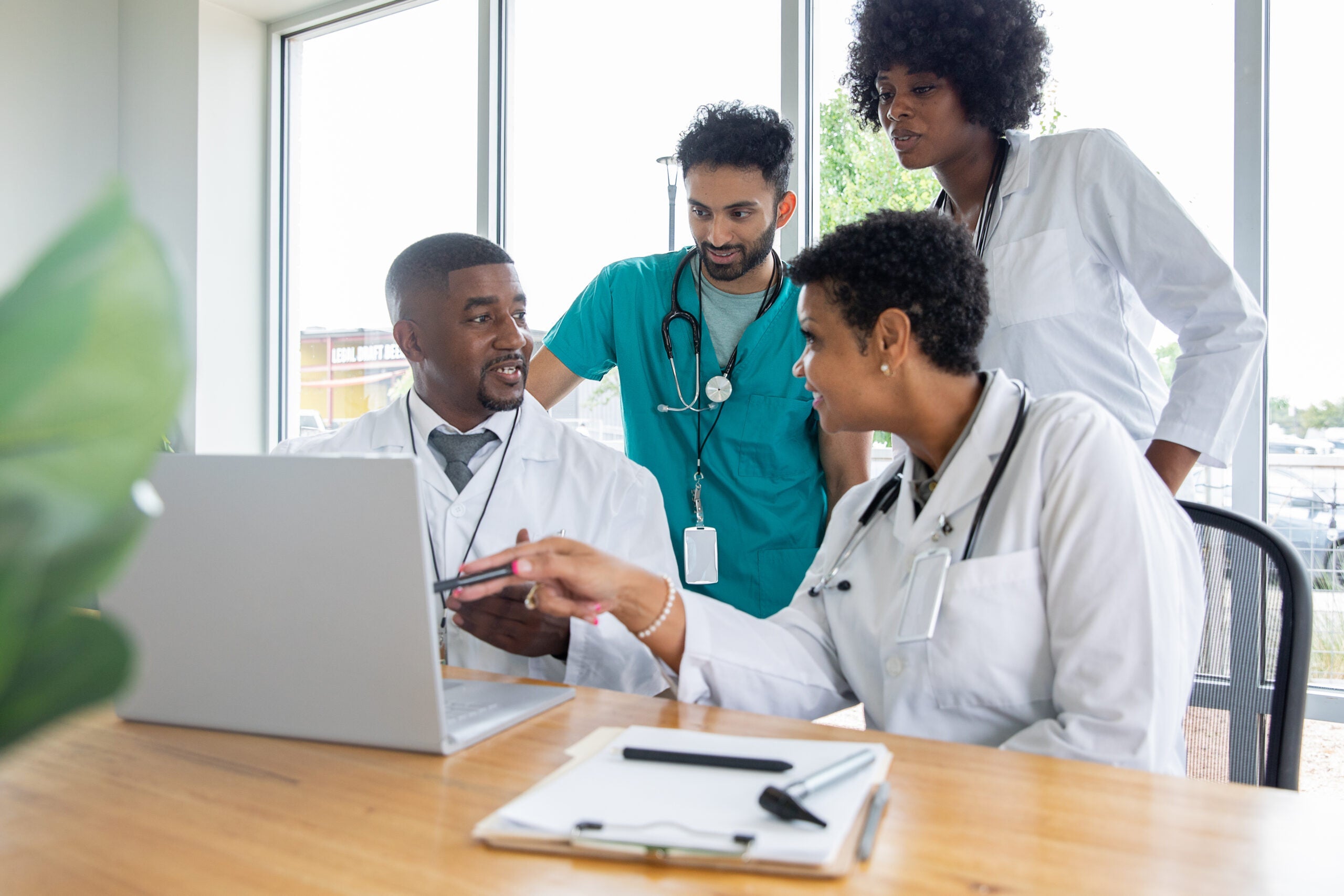 A group of hospital staff in a meeting room, huddled around a laptop on a table, talking.