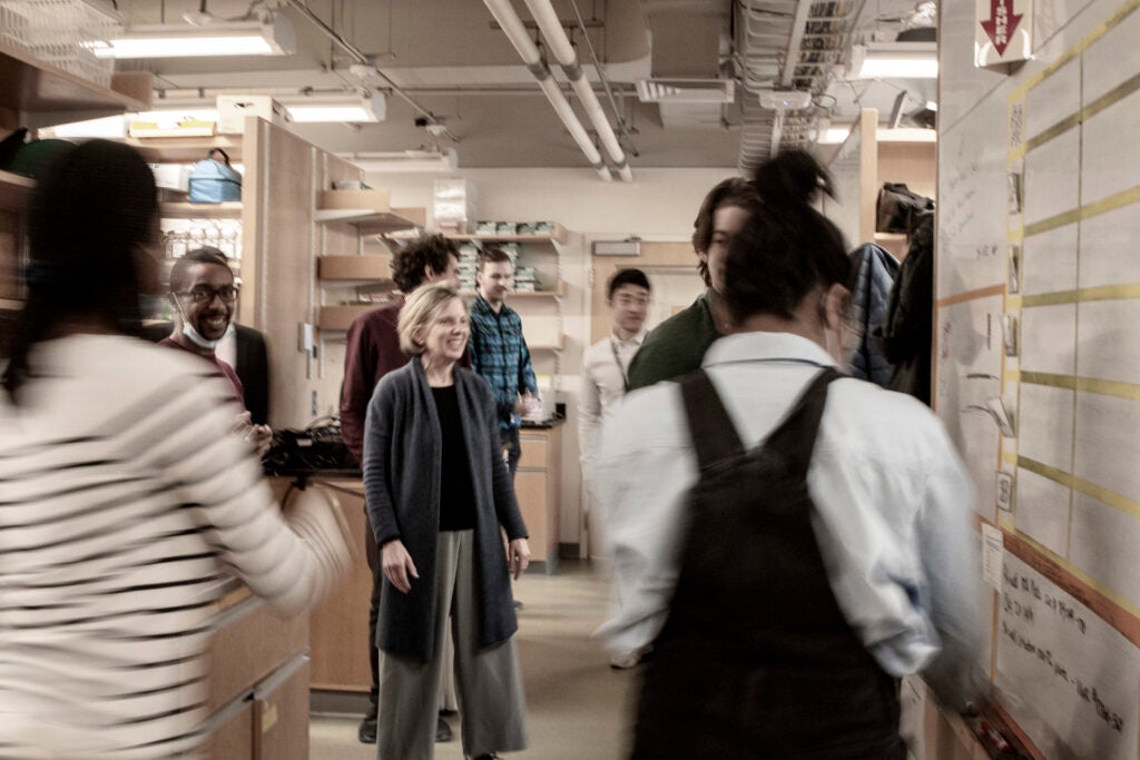 Lab members surrounding Sarah Fortune while in the lab. Lab members are all talking and laughing with one another. 