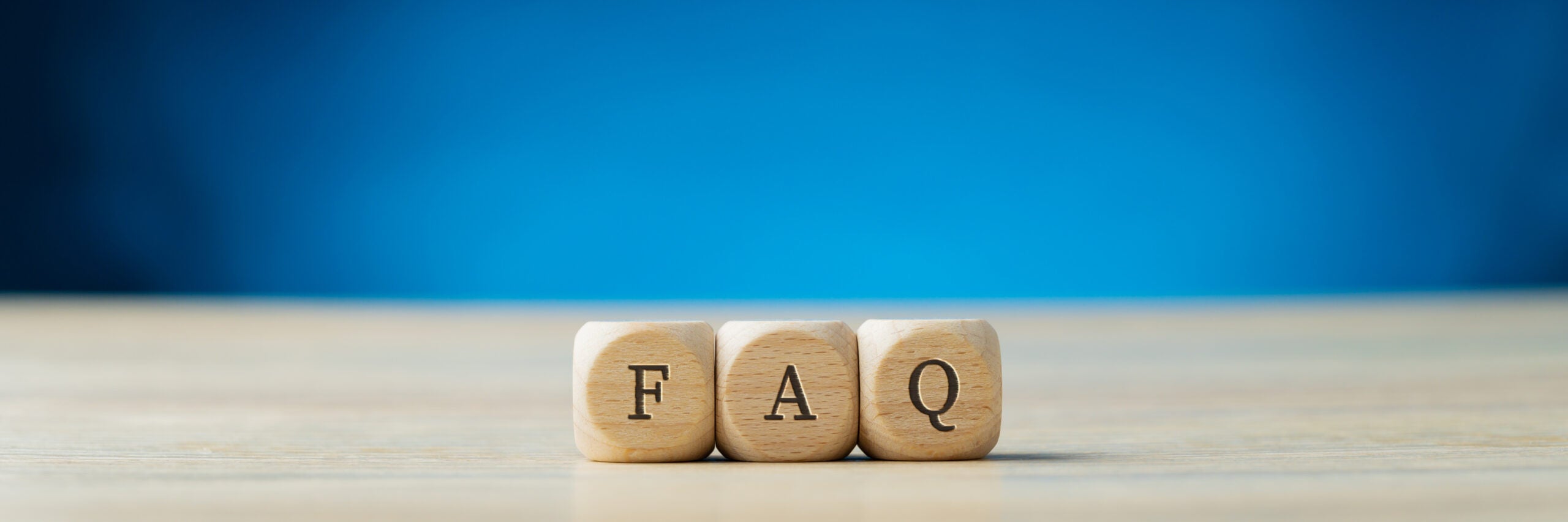 Three wooden blocks with the letters "F," "A," and "Q" arranged in a row on a wooden surface, with a gradient blue background. The blocks symbolize Frequently Asked Questions.