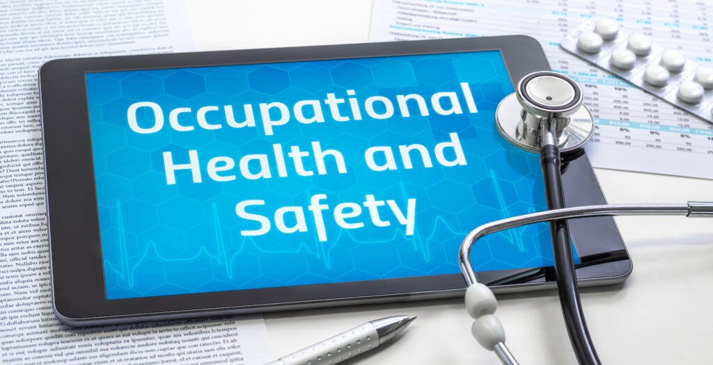 Tablet displaying the words 'Occupational Health and Safety' surrounded by a stethoscope, medical documents, a pen, and a blister pack of pills.