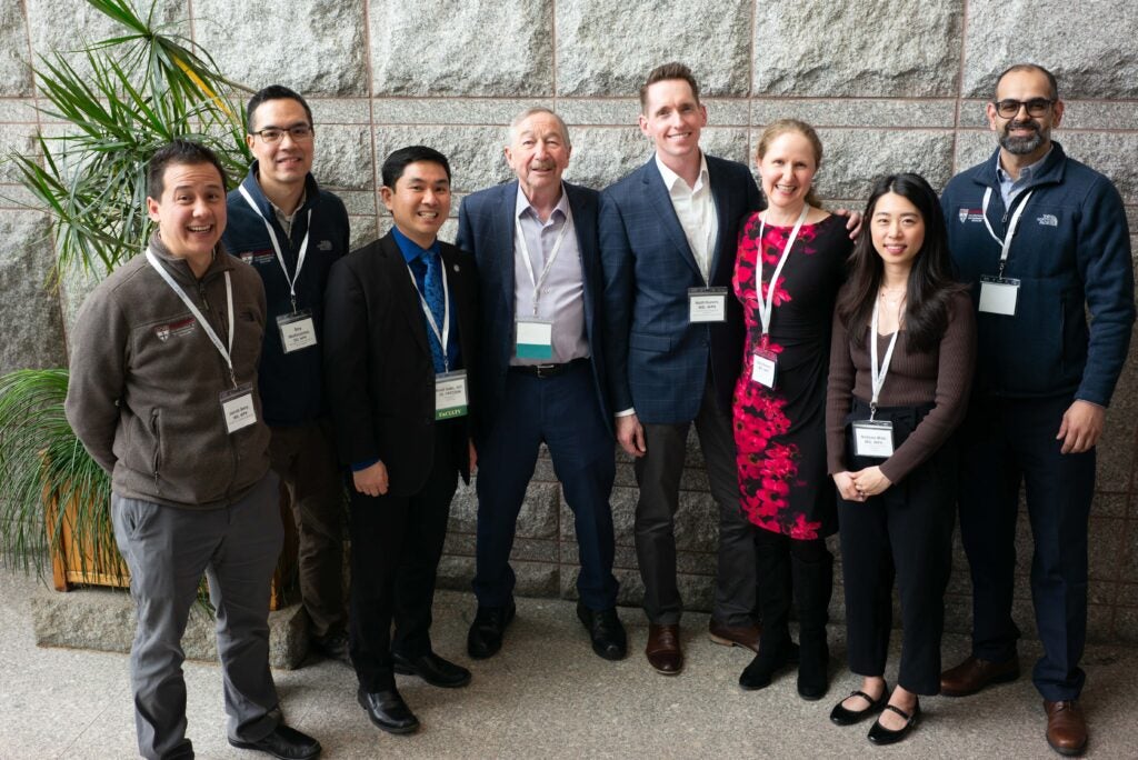 Group of people wearing name tags and lanyards, posing for a photo in front of a stone wall at an indoor event.