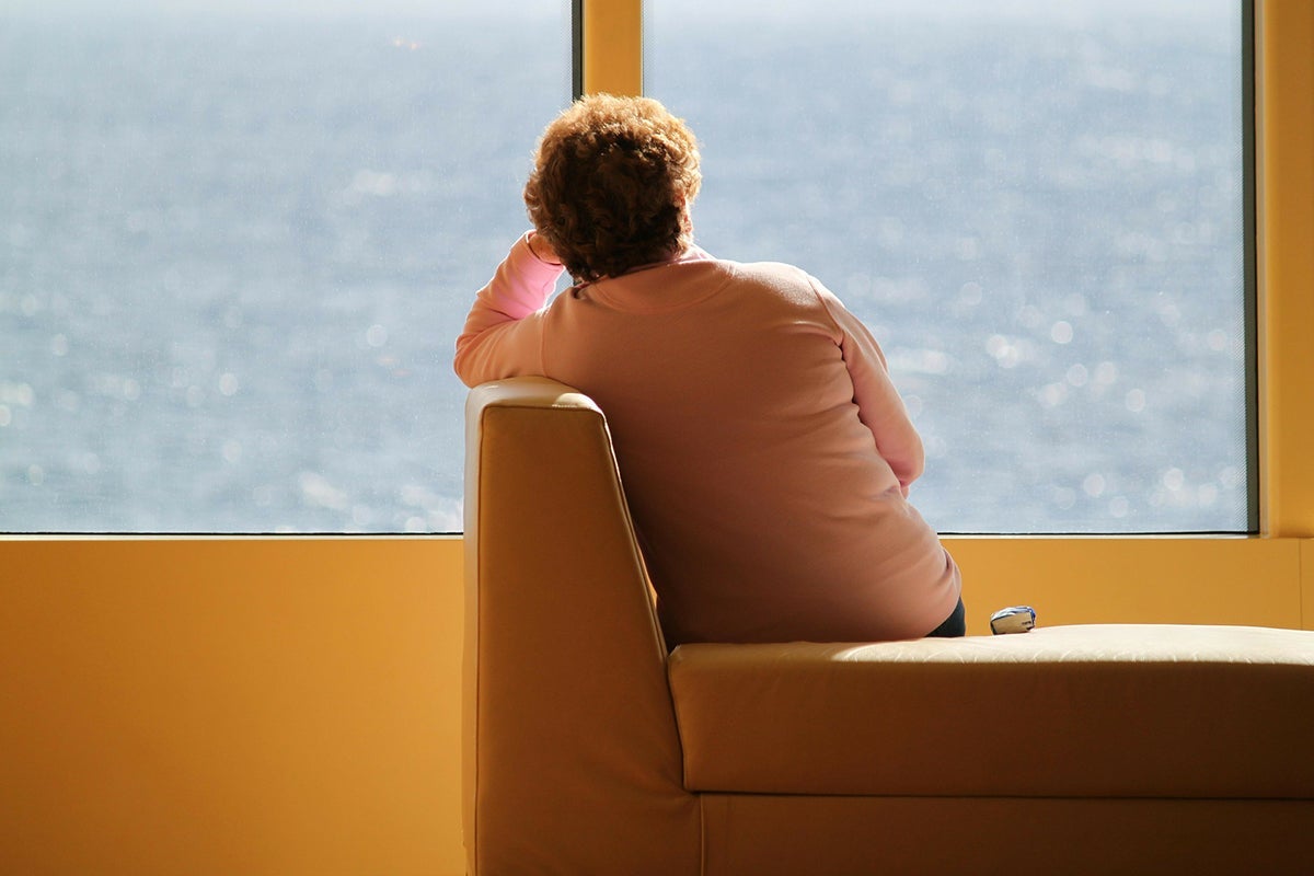 Lonely woman, from rear, looking out window at water