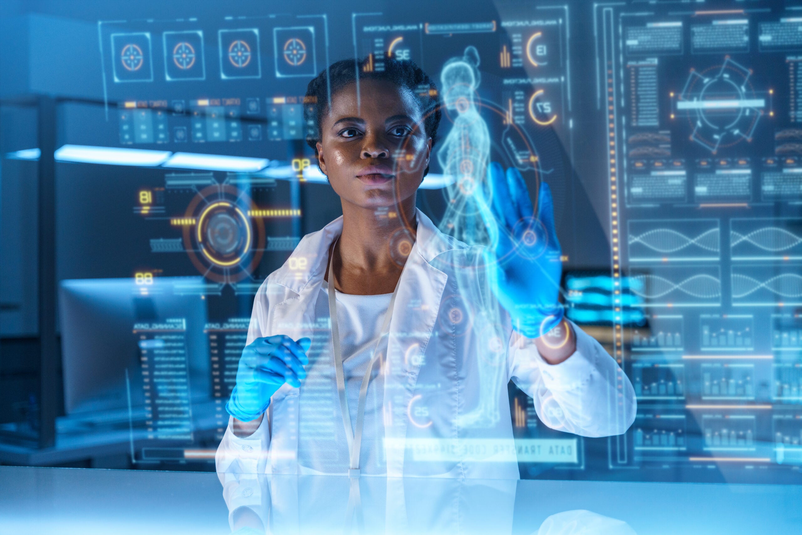 A female healthcare professional wearing a lab coat and blue gloves interacts with a holographic display showing a digital human anatomy model and various medical data points. The futuristic interface includes graphs, charts, and diagnostic metrics, symbolizing the use of advanced AI and digital tools in clinical healthcare settings.