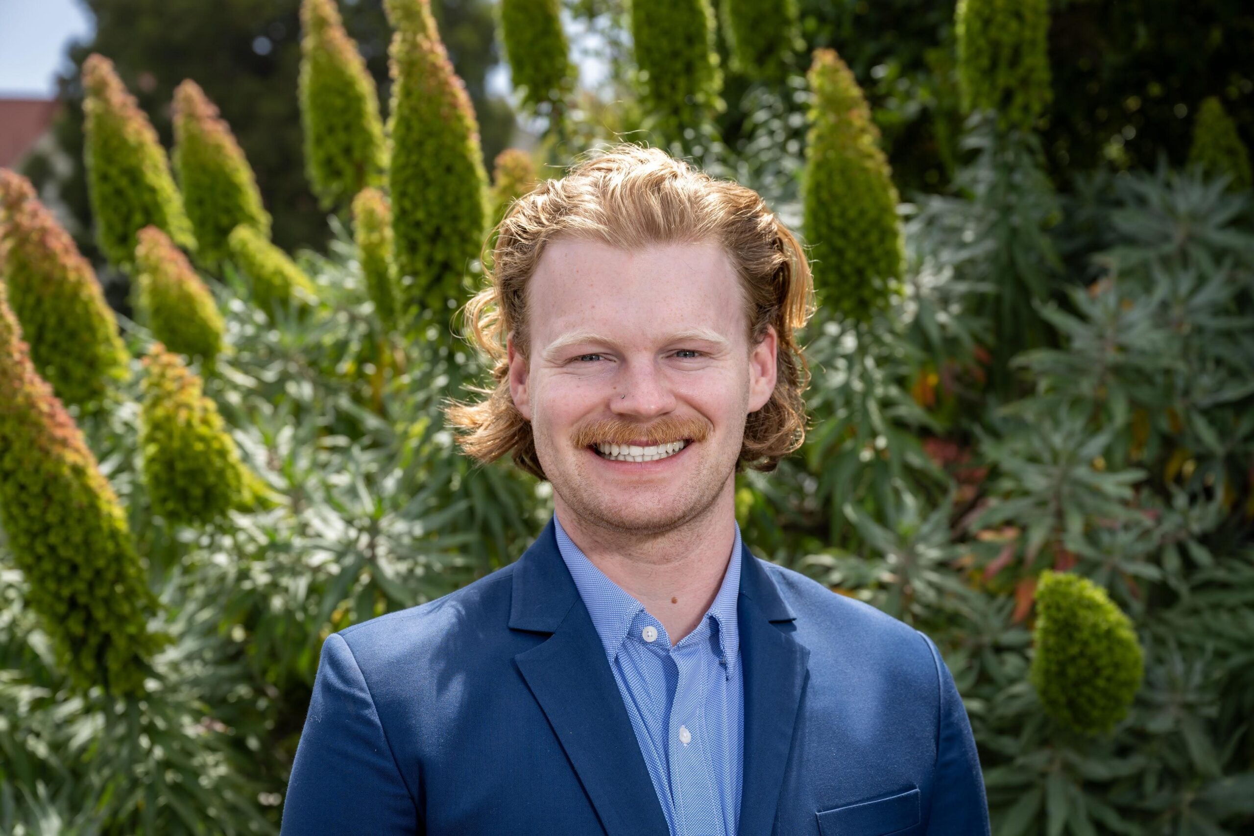 a headshot of Jonathan Gilmour. He is outside and the background is full of tall green plants.
