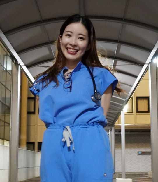 a picture of Dr. Lisa Yamasaki. She has dark brown hair that goes just past her shoulders and she is wearing blue scrubs. she smiles at the camera and her hands are behind her back.