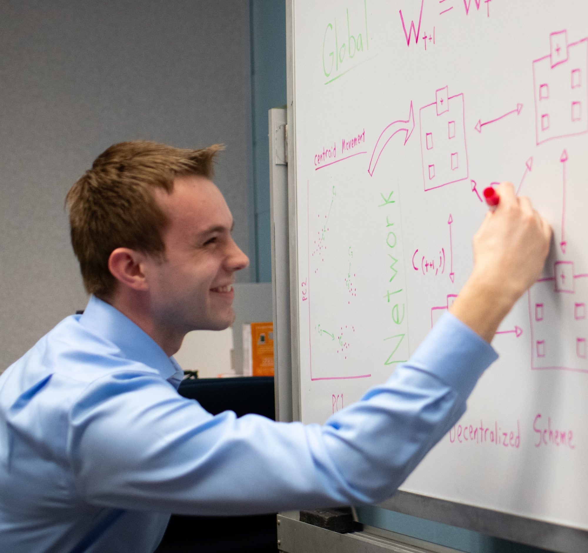 a photo of Salvador Balkus. He is smiling, writing on a whiteboard with a red marker.
