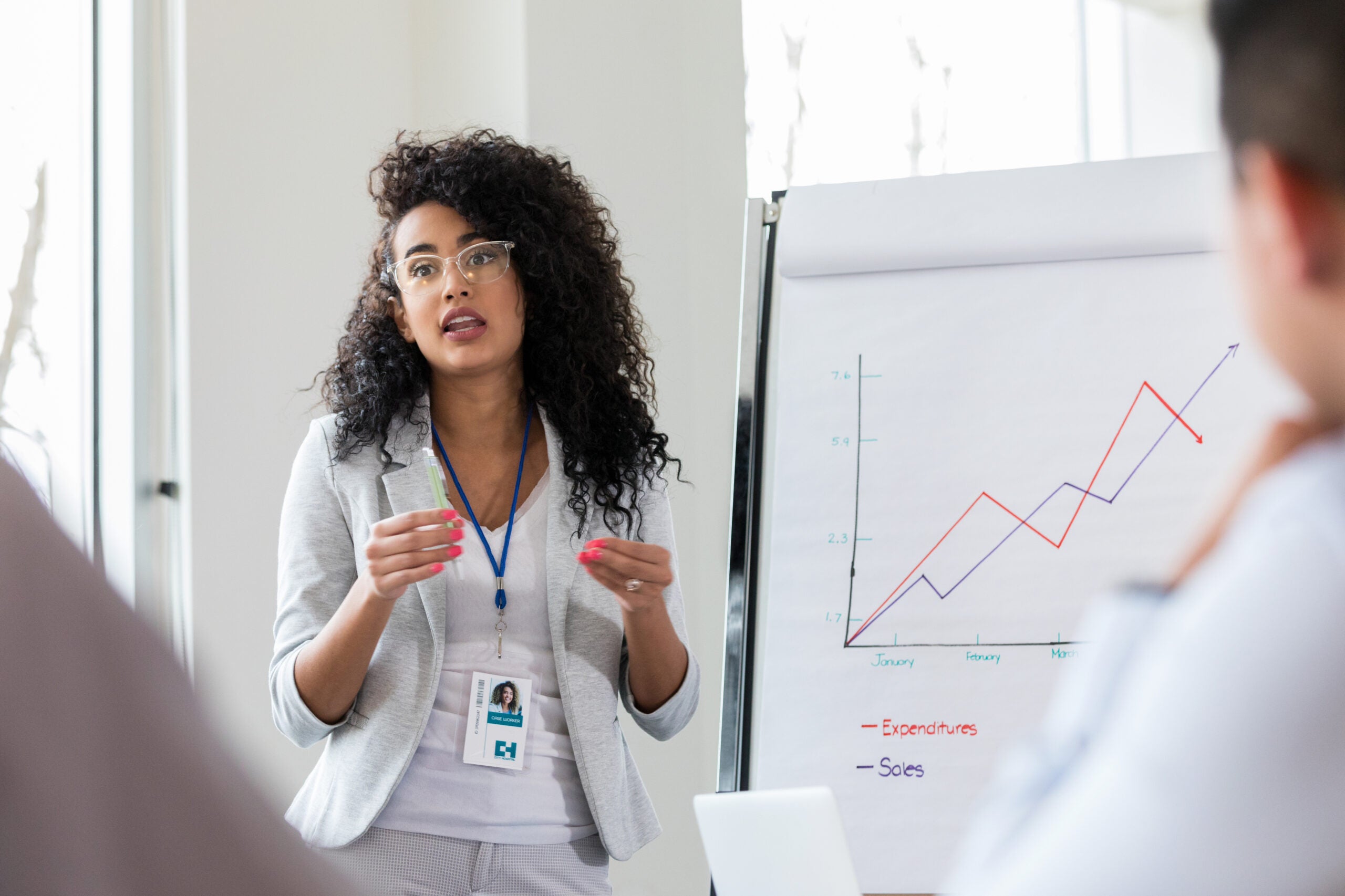 A businesswoman delivers a presentation in front of a chart showcasing sales growth.
