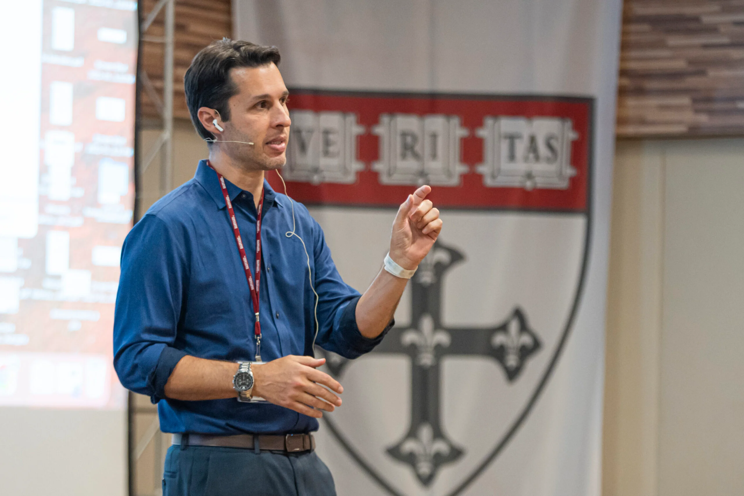 Professor Felipe Fregni delivering a lecture in front of a Harvard tapestry