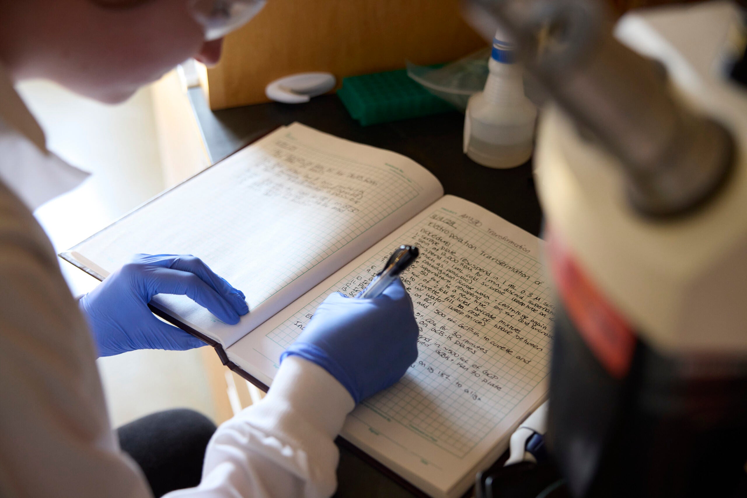 Grad lab member writes in notebook while at the lab bench.