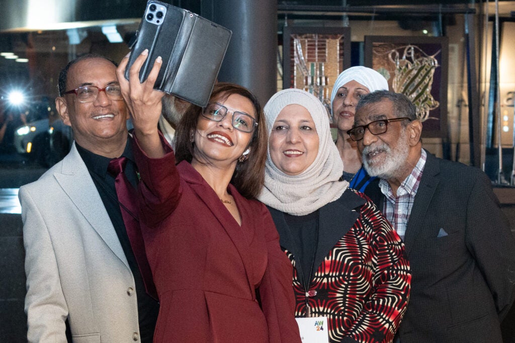 A group of men and women lean back to take a selfie. They are wearing coordinated formal outfits in shades of crimson, taupe, and black.
