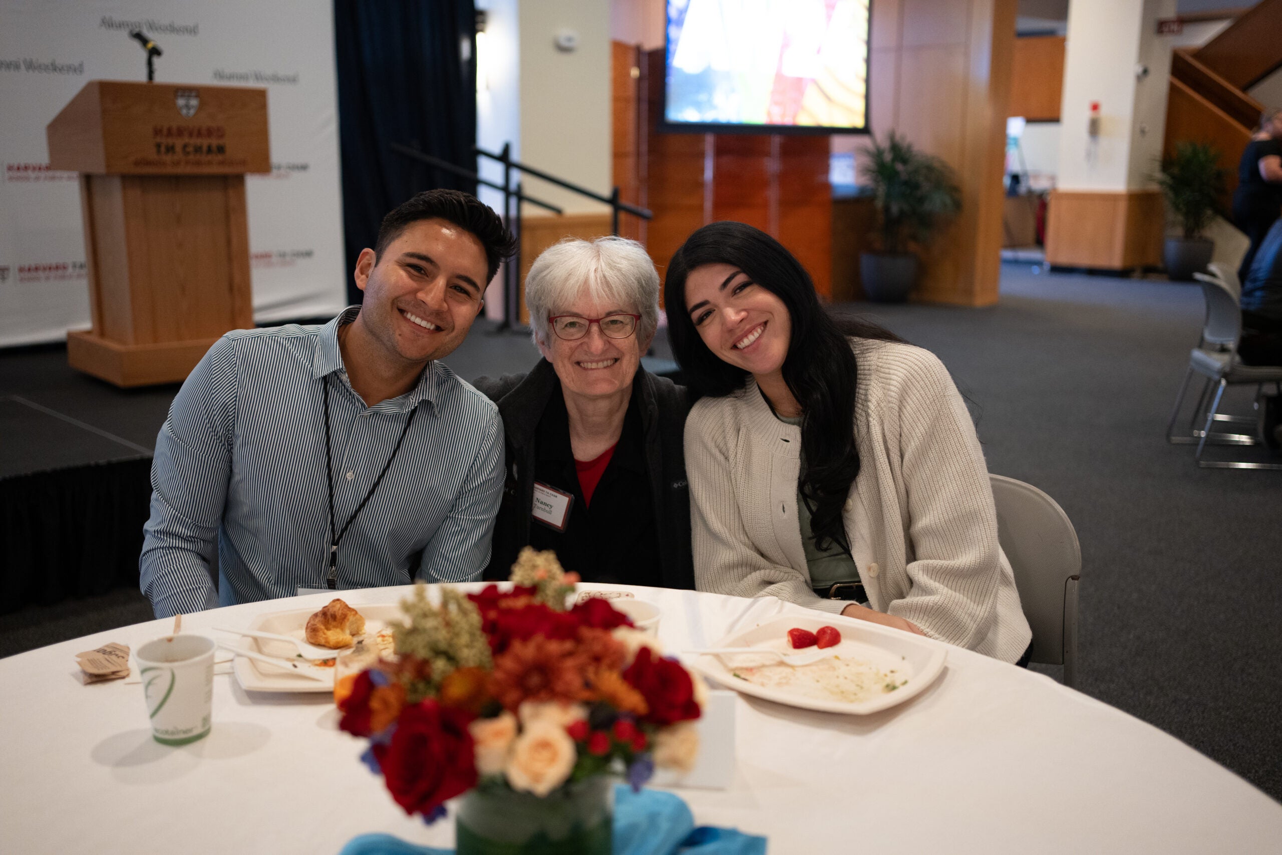 Senior Associate Dean for Educational Programs Nancy Turnbull poses seated at a table between a young man and a young woman. All have big smiles.