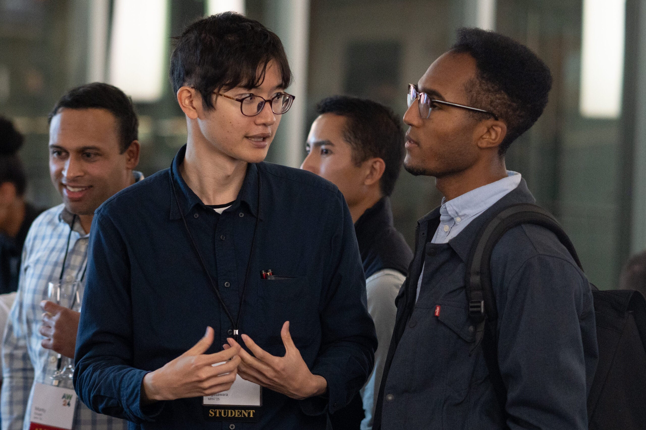 Among the throng of alumni weekend guests, a student in a navy button-down shirt is gesturing while speaking to another guest shown in profile.