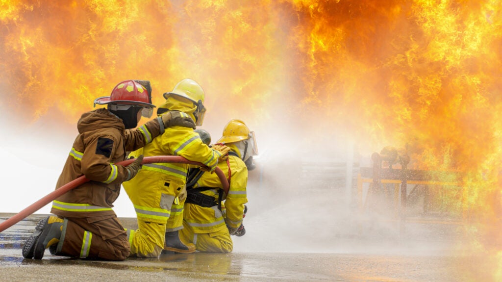 Three firefighters using a fire hose to extinguish flames.