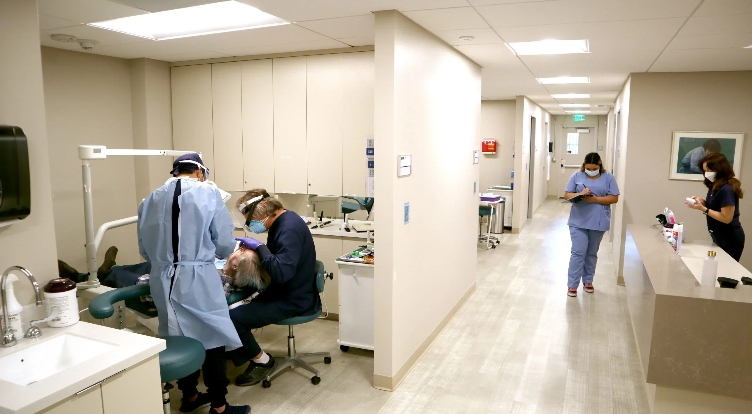 Masked clinic workers provide dental services to a patient