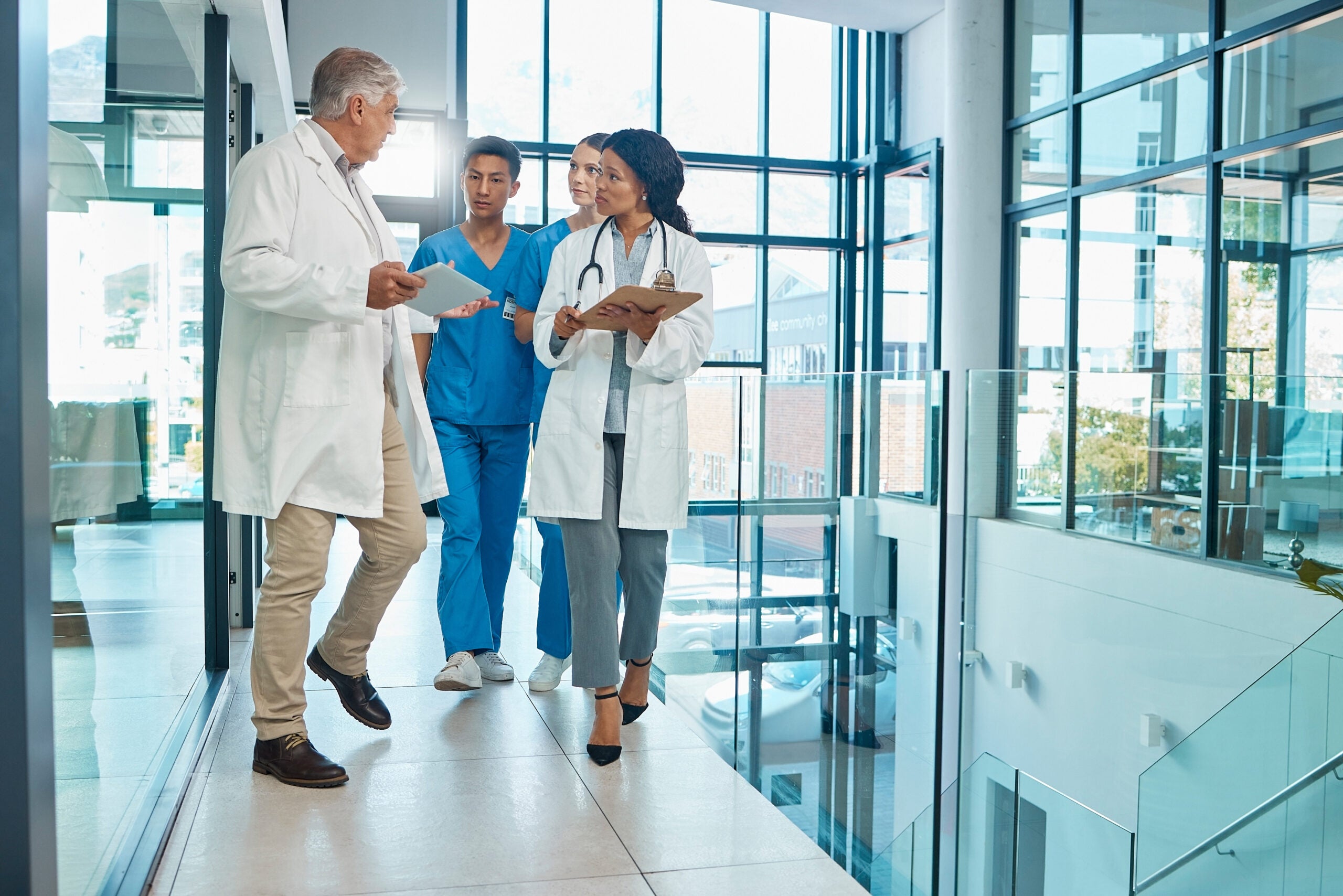 Two doctors and two nurses walking down a hallway, as the male doctor speaks to the team.