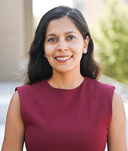 A photo of Nandita Perumal smiling in a crimson colored outfit