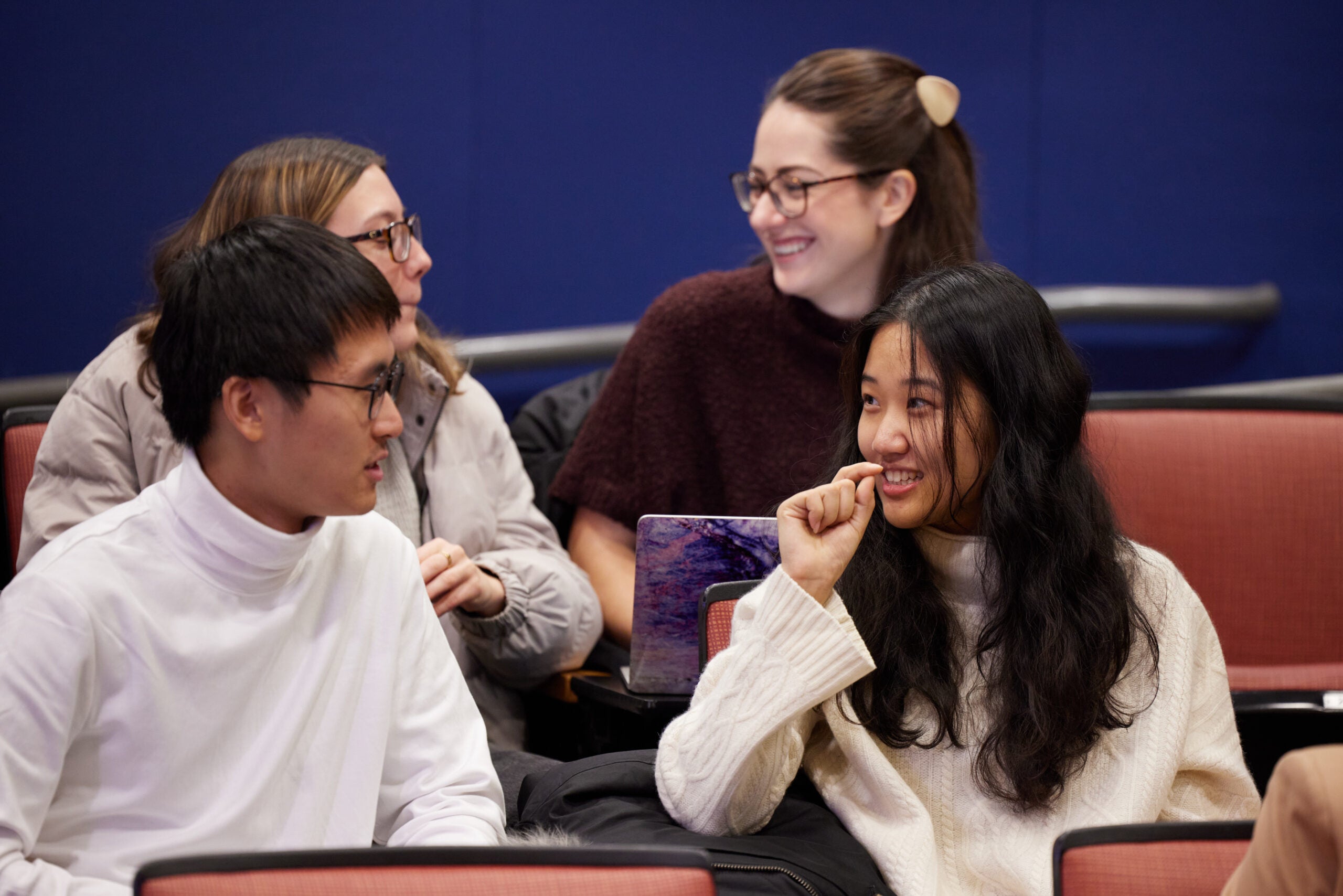 A group of four students laugh and talk in a classroom. 