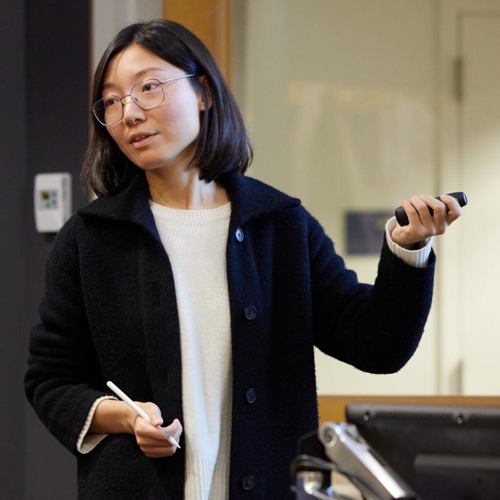 Professor Rui Duan looks to the left of the frame, holding a stylus in one hand and slide advancer in the other.