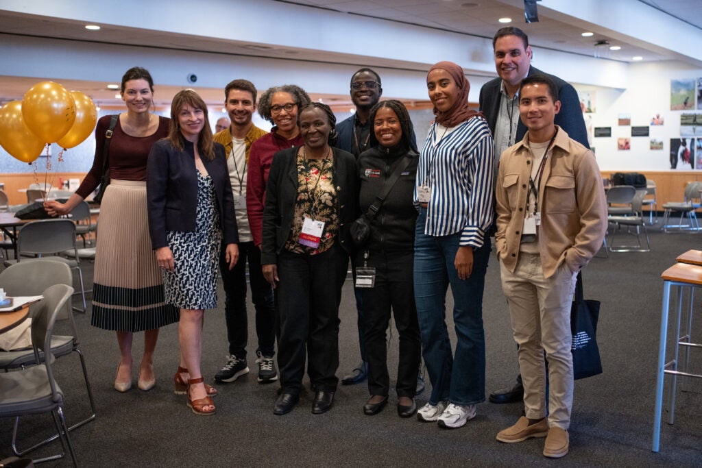 A group of ten people poses, smiling. They appear to be of diverse ages and racial backgrounds, though many look like they could be students.