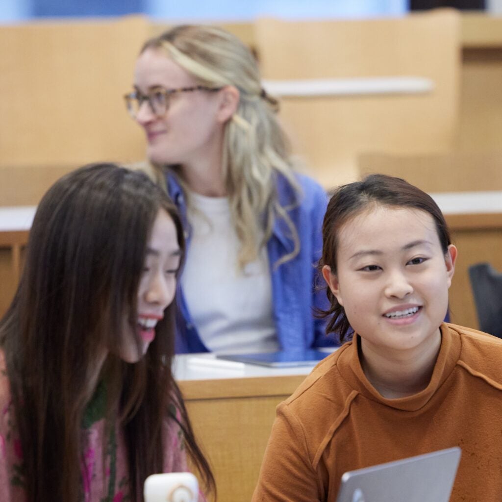 Students in a lecture hall talk and laugh with one another. 