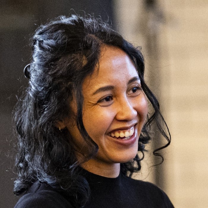 Headshot of a woman with dark, wavy, shoulder-length hair half pulled back, smiling and looking out the right of the frame. 