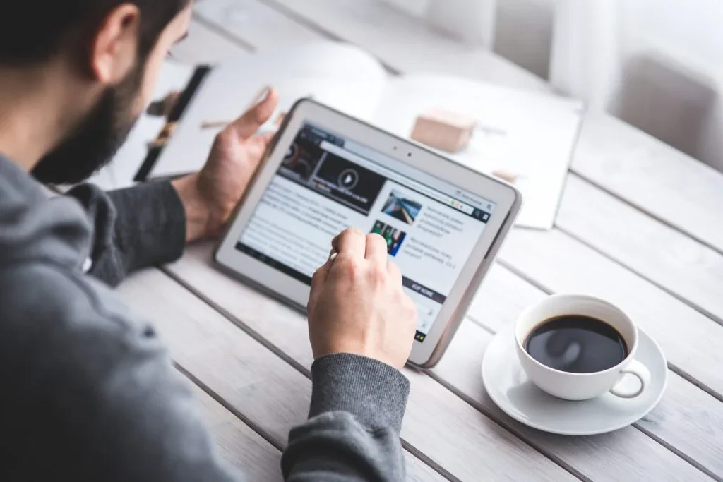 Person sitting at a table with a cup of coffee, holding an iPad and browsing the news