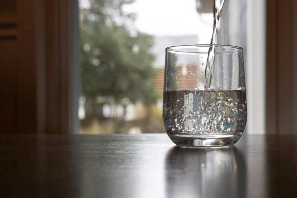 A glass of drinking water being filled at a tap inside of a home.