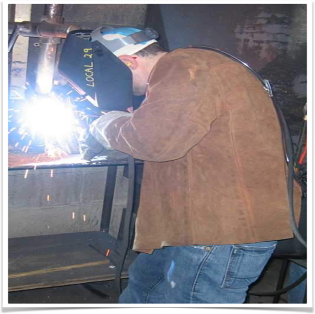 A man welds a piece of metal while wearing a welding mask.