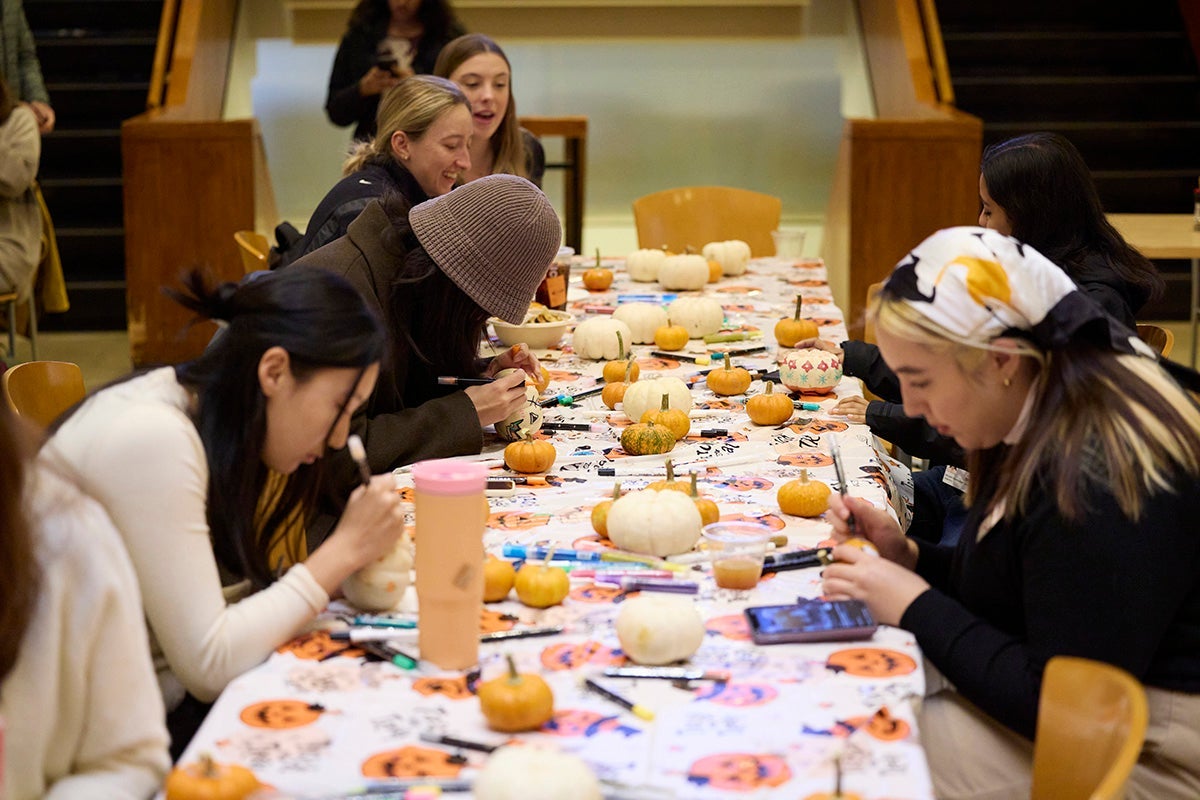 Students painting pumpkins at table.