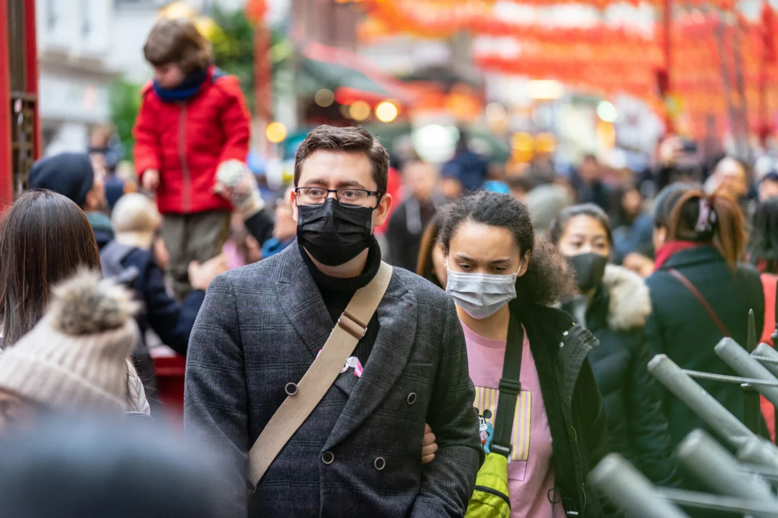 A couple walking through a crowded outdoor space wearing masks